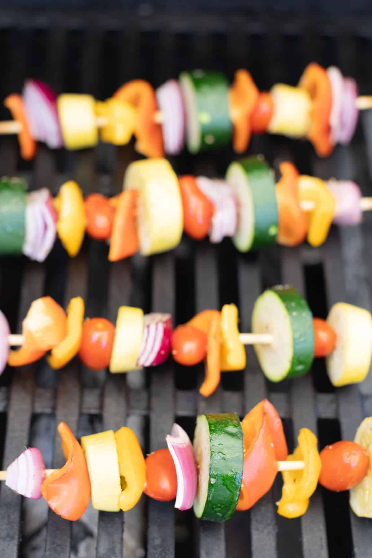 Close-up of colorful vegetable skewers with zucchini, bell peppers, cherry tomatoes, and onions on a grill.