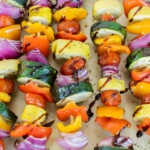 A tray of grilled vegetable skewers with zucchini, bell peppers, cherry tomatoes, and red onions, drizzled with balsamic glaze.