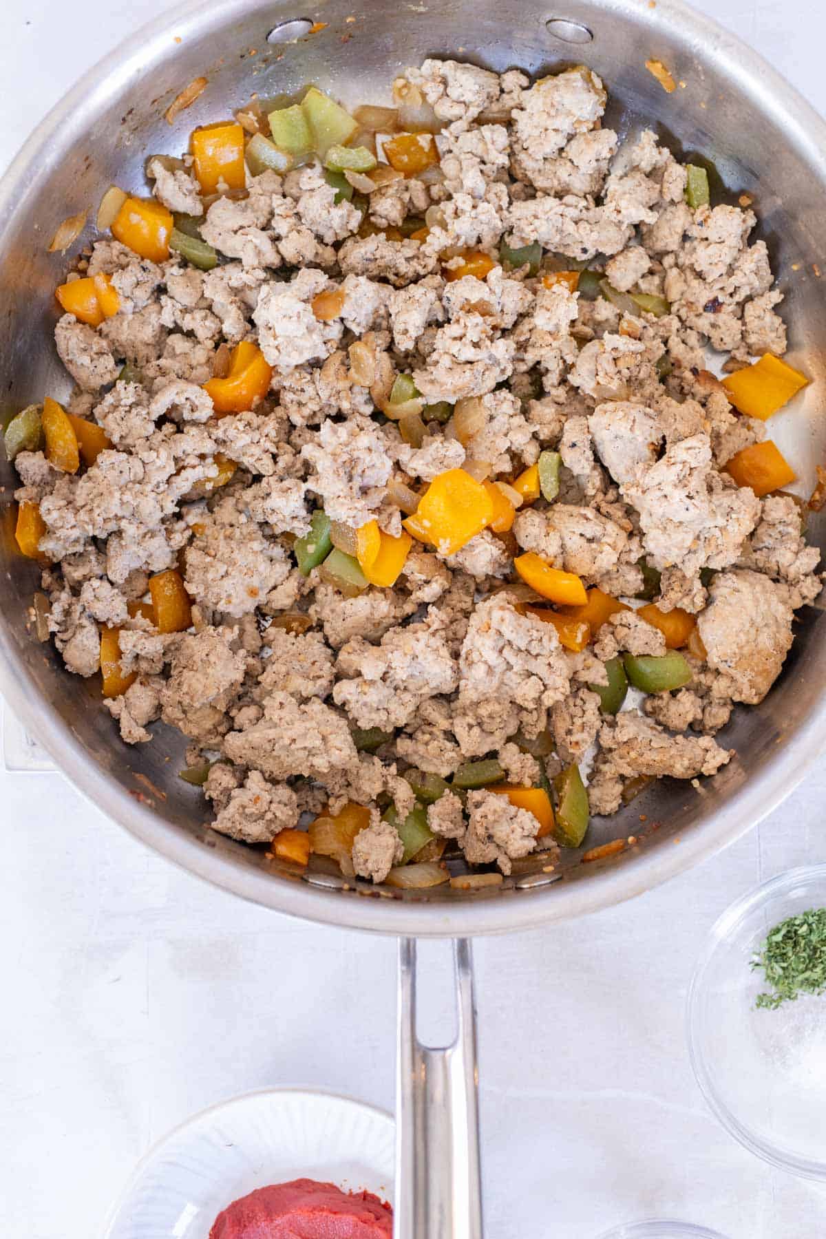 A stainless steel pan containing cooked ground turkey mixed with diced yellow and green bell peppers.