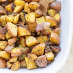 A white dish filled with roasted breakfast potatoes, mixed with herbs and a wooden spoon for serving.