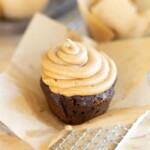 A chocolate muffin with peanut butter frosting sits on parchment paper atop a wire cooling rack.