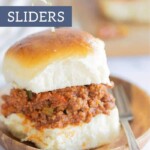 Close-up of delectable Sloppy Joe Sliders on a wooden plate with a fork on the side. Text at the top reads "Sloppy Joe Sliders.