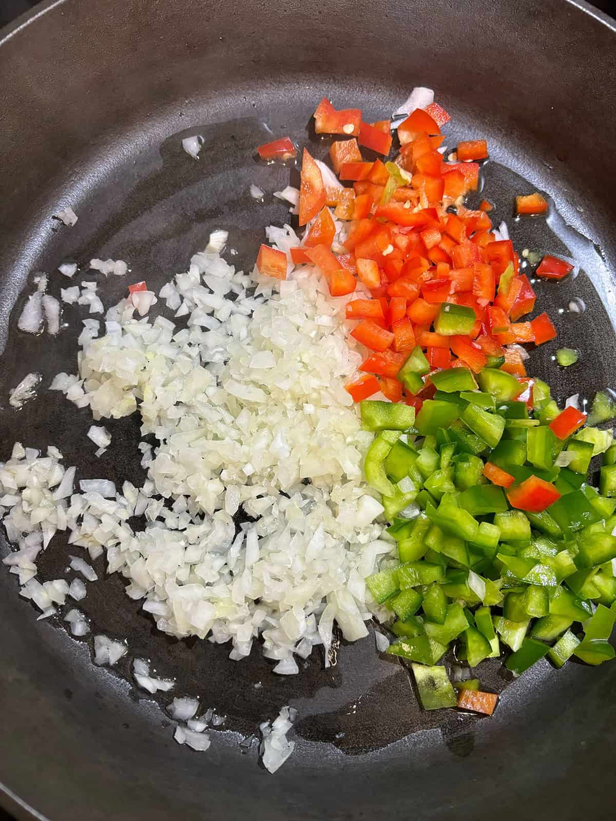 Chopped onions, red bell peppers, and green bell peppers being saut&eacute;ed in a pan with oil for delicious Sloppy Joe Sliders.