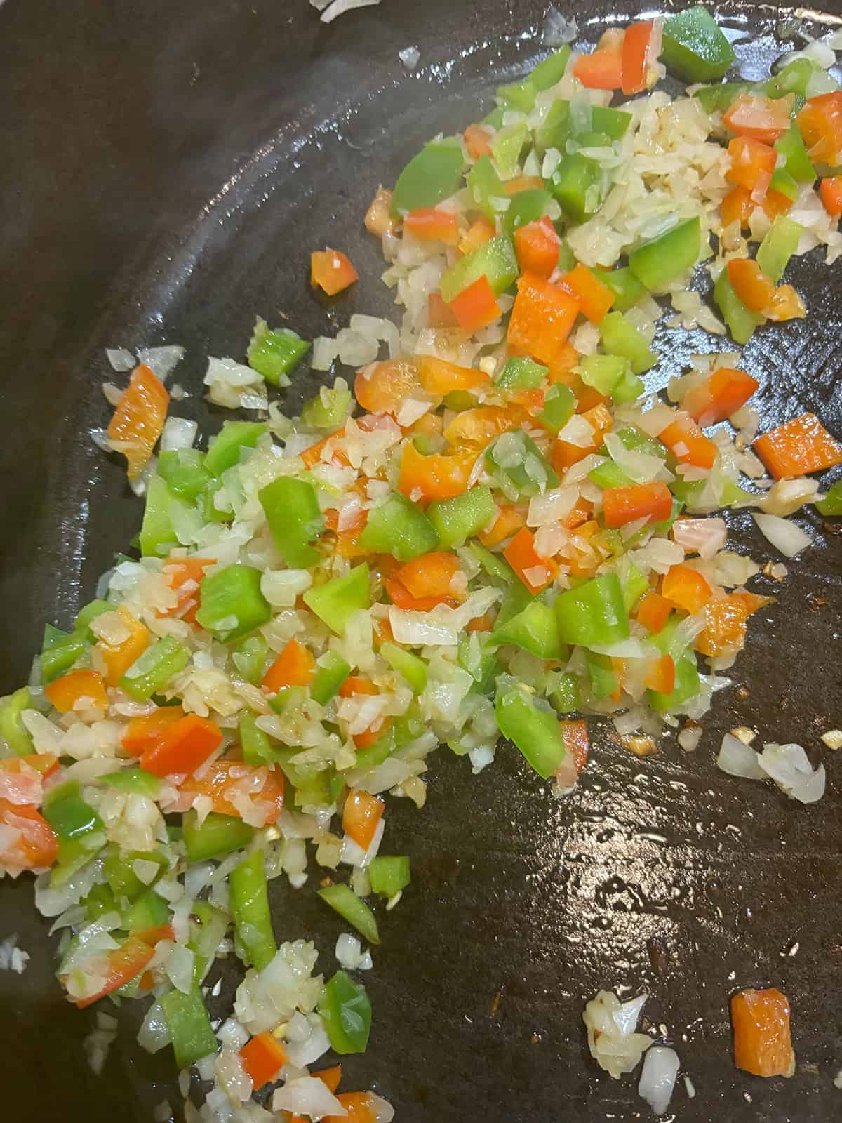 Diced green and red bell peppers and onions are saut&eacute;ing in a dark-colored frying pan, adding a flavorful base for mouthwatering Sloppy Joe Sliders.
