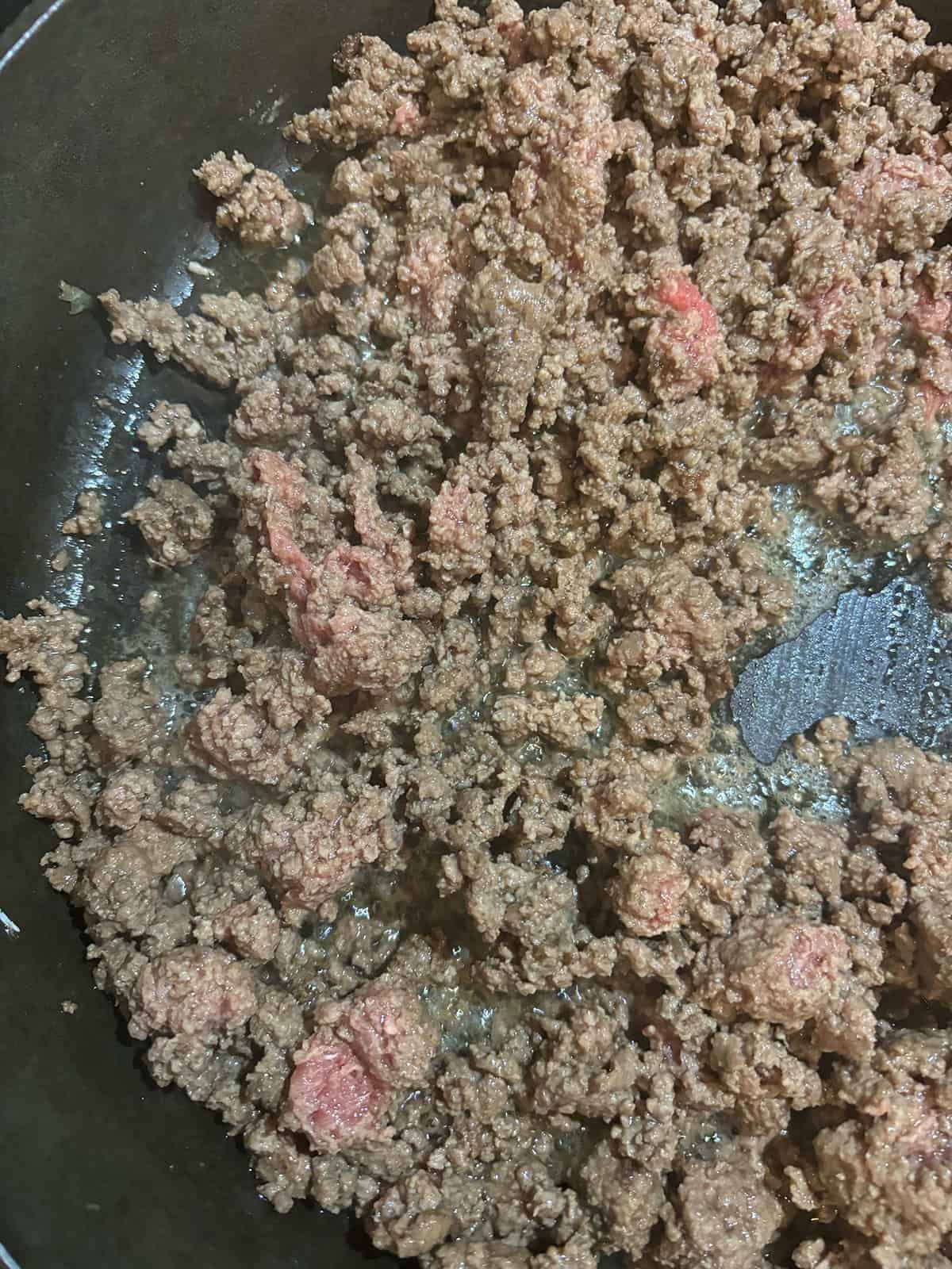 Ground beef cooking in a dark skillet, partially browned with some pink areas still visible, perfect for making Sloppy Joe Sliders.