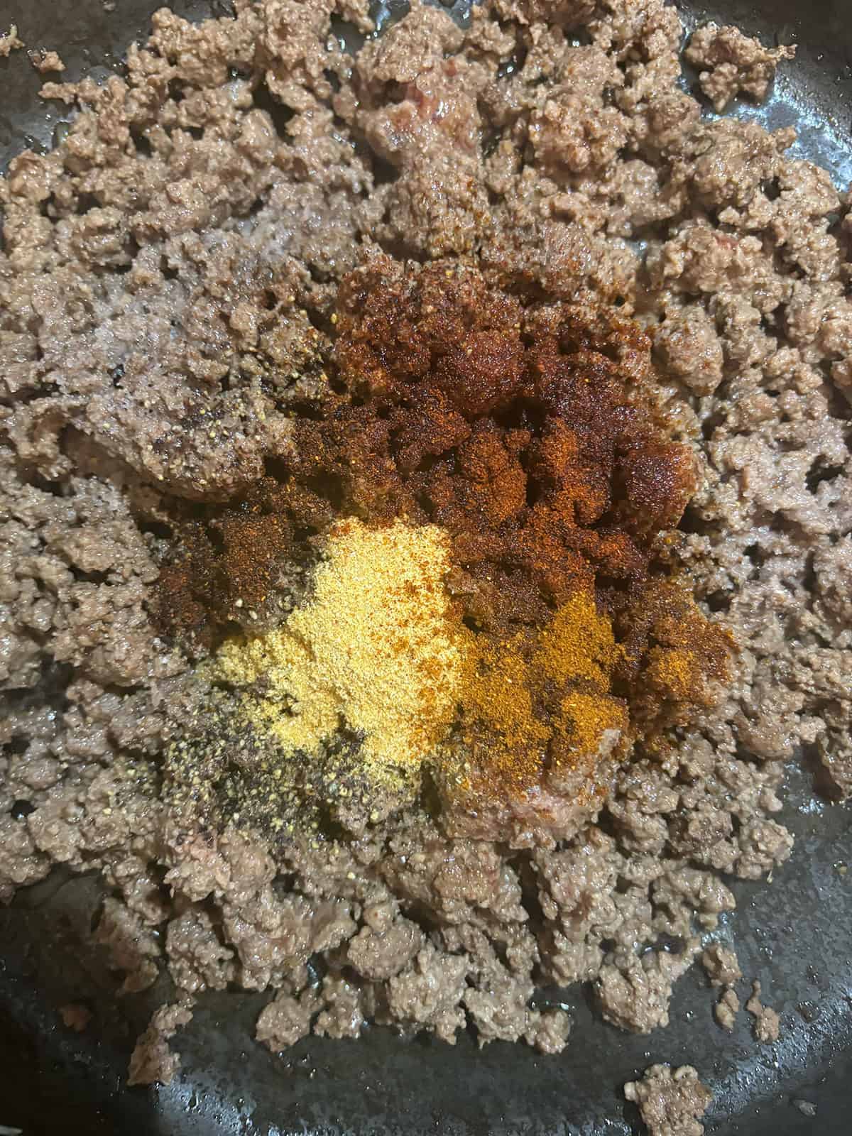Ground meat sizzles in a pan as various spices, including yellow, red, and brown powders, blend together. Perfect for creating mouthwatering Sloppy Joe Sliders.