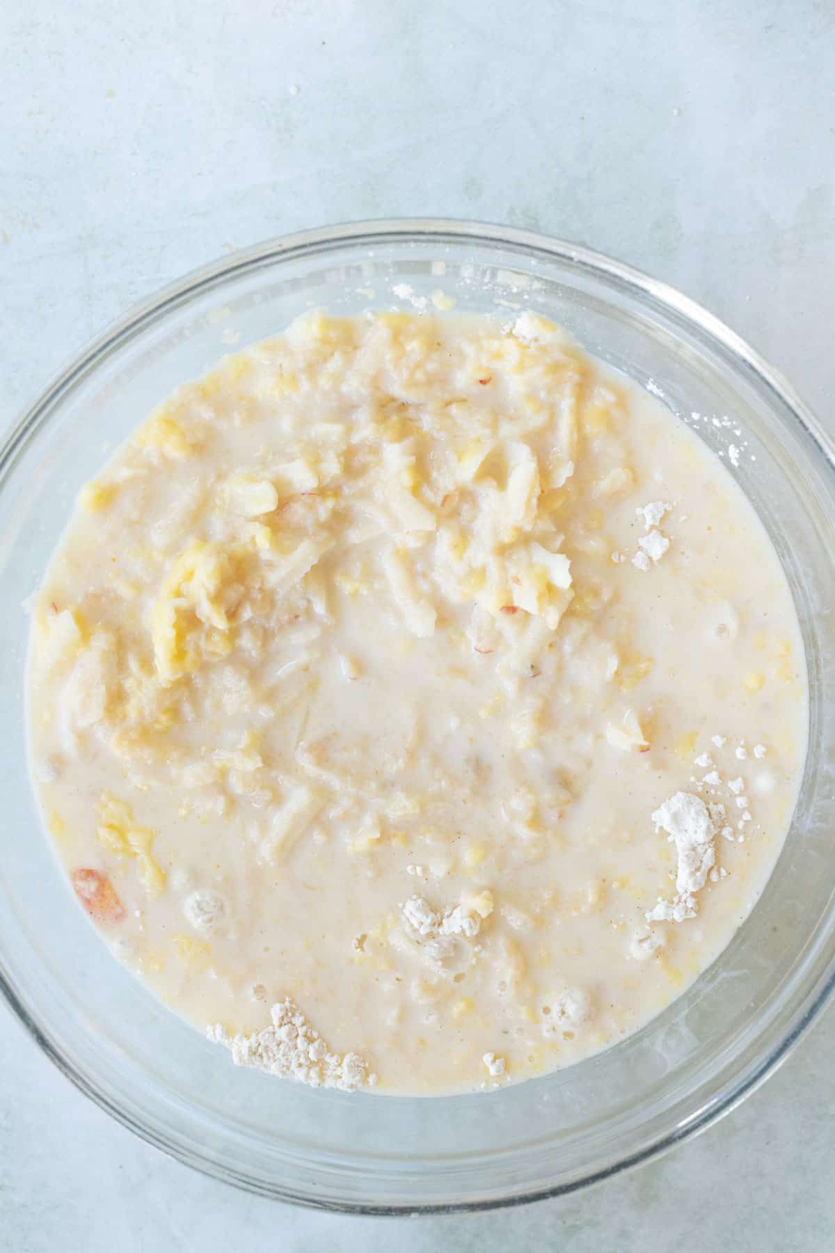 A bowl of mixed ingredients, including apple pancake batter, is set on a light-colored countertop.