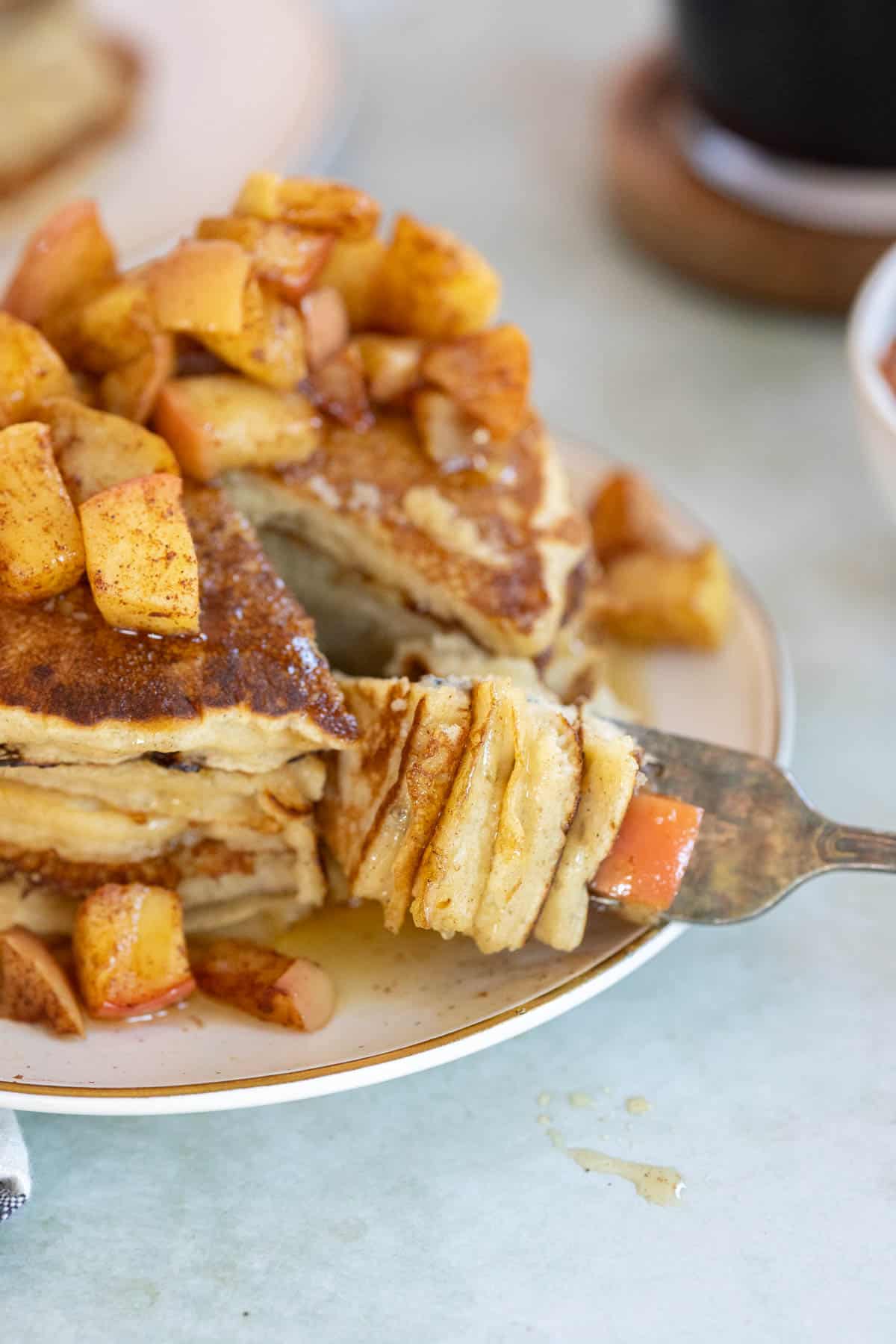 A fork holding a sliced portion apple pancakes on the side.