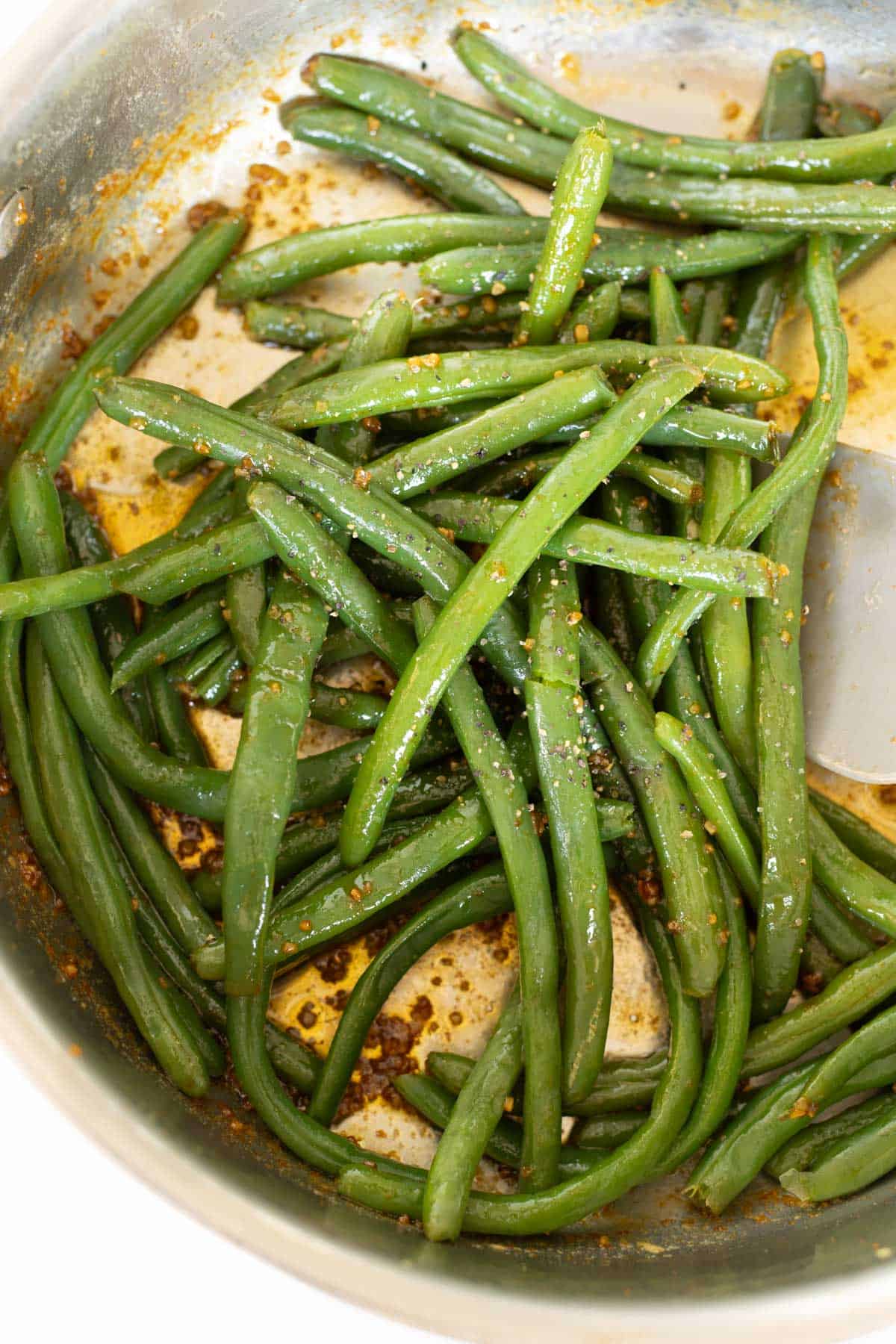 A pan filled with cooked, asian green beans seasoned with spices and oil.