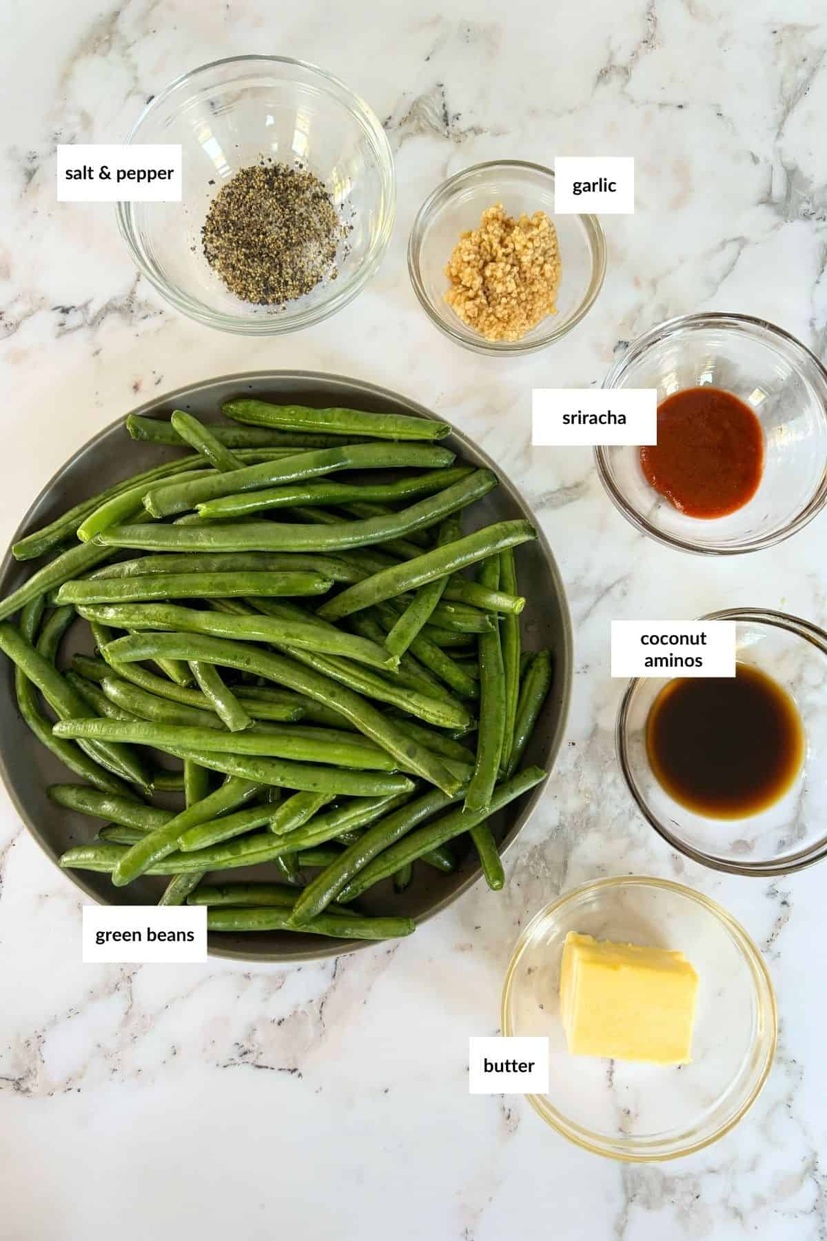 Asian greens on a marble surface: green beans, salt & pepper, minced garlic, sriracha, coconut aminos, and a block of butter in small bowls.