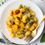 A plate of cornbread stuffing with herbs and vegetables, accompanied by a gold fork.