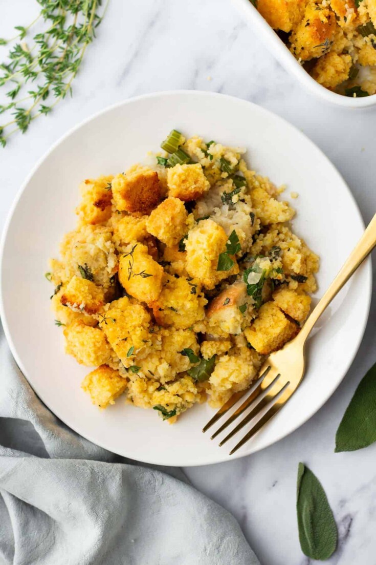 A plate of cornbread stuffing with herbs and vegetables, accompanied by a gold fork.