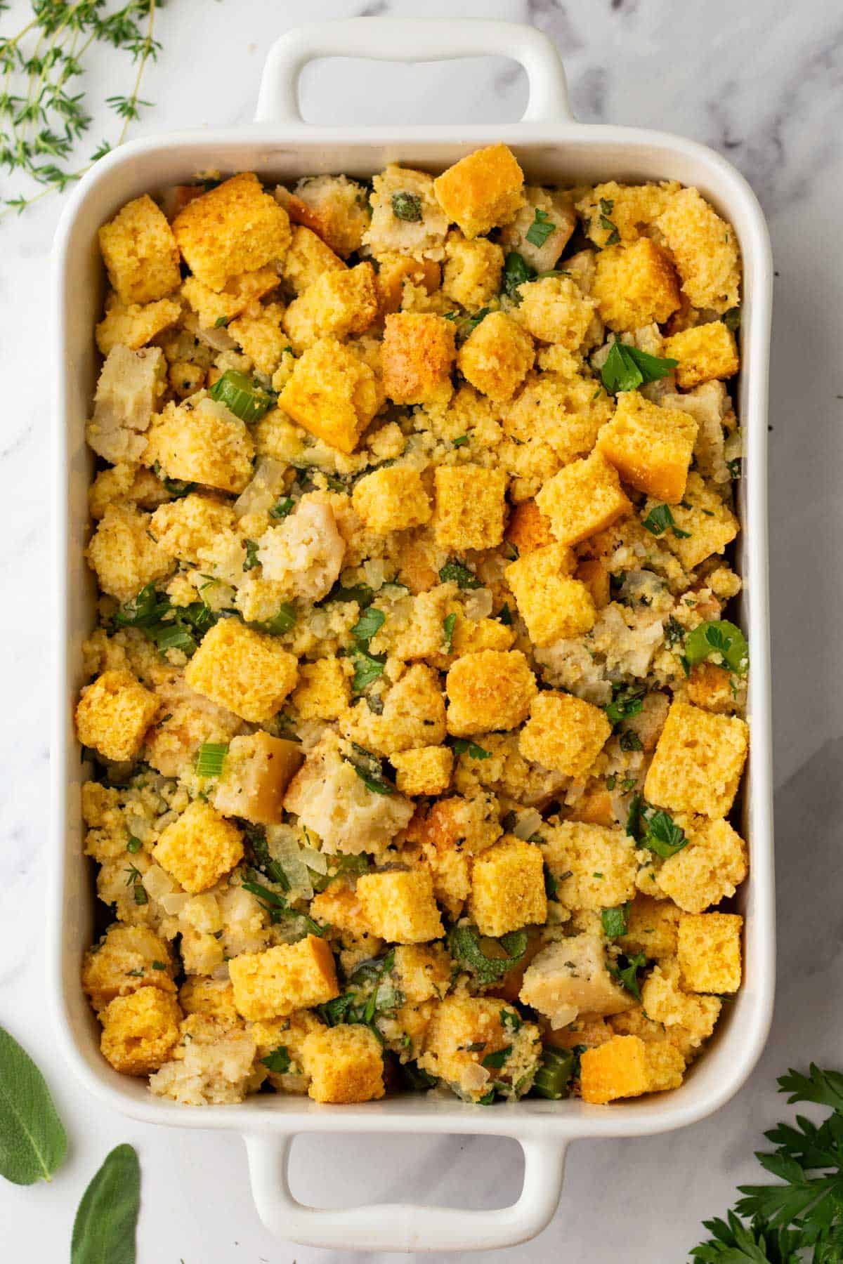 A white baking dish filled with cornbread stuffing mixed with herbs and vegetables.