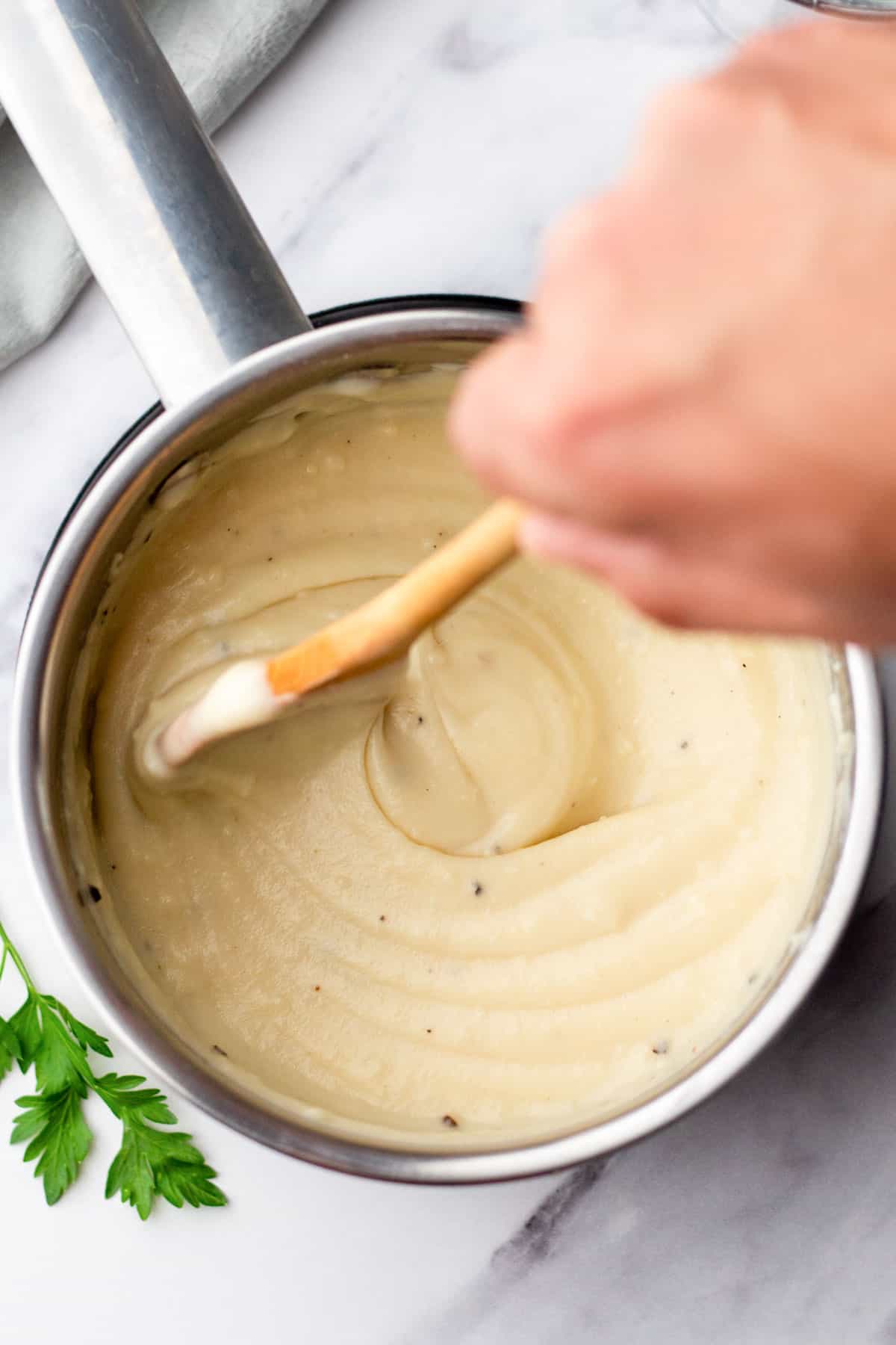 Hand stirring cream of chicken in a pot with a wooden spoon, garnished with parsley on the side.