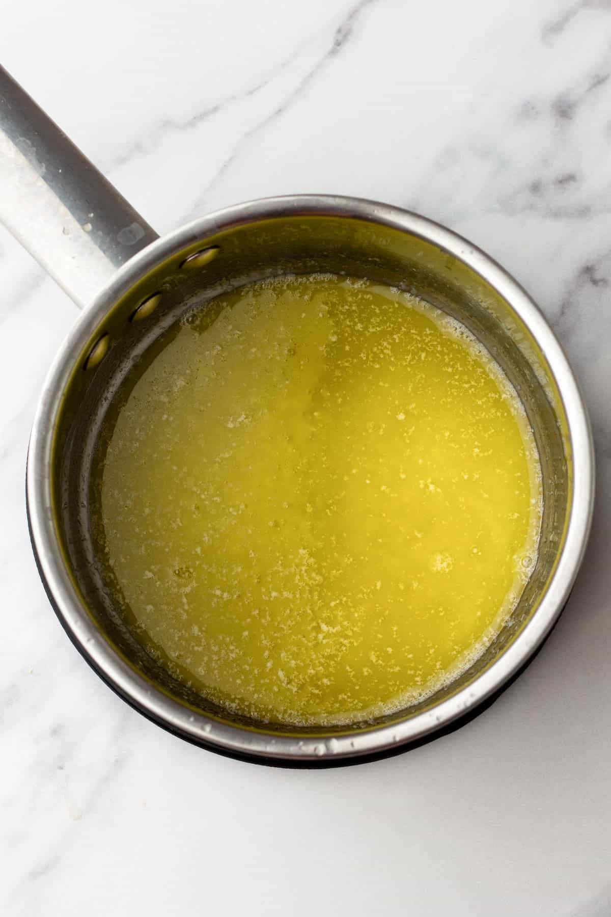 Melted butter in a metal saucepan on a marble countertop.