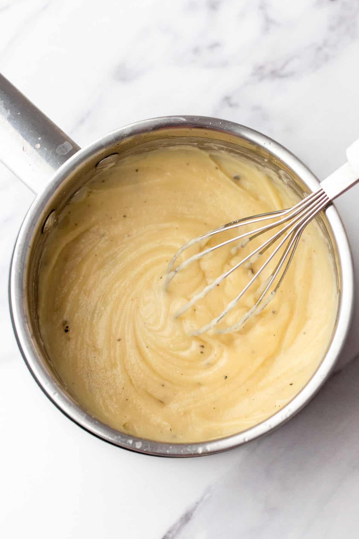 A saucepan filled with cream of chicken being whisked on a marble countertop.