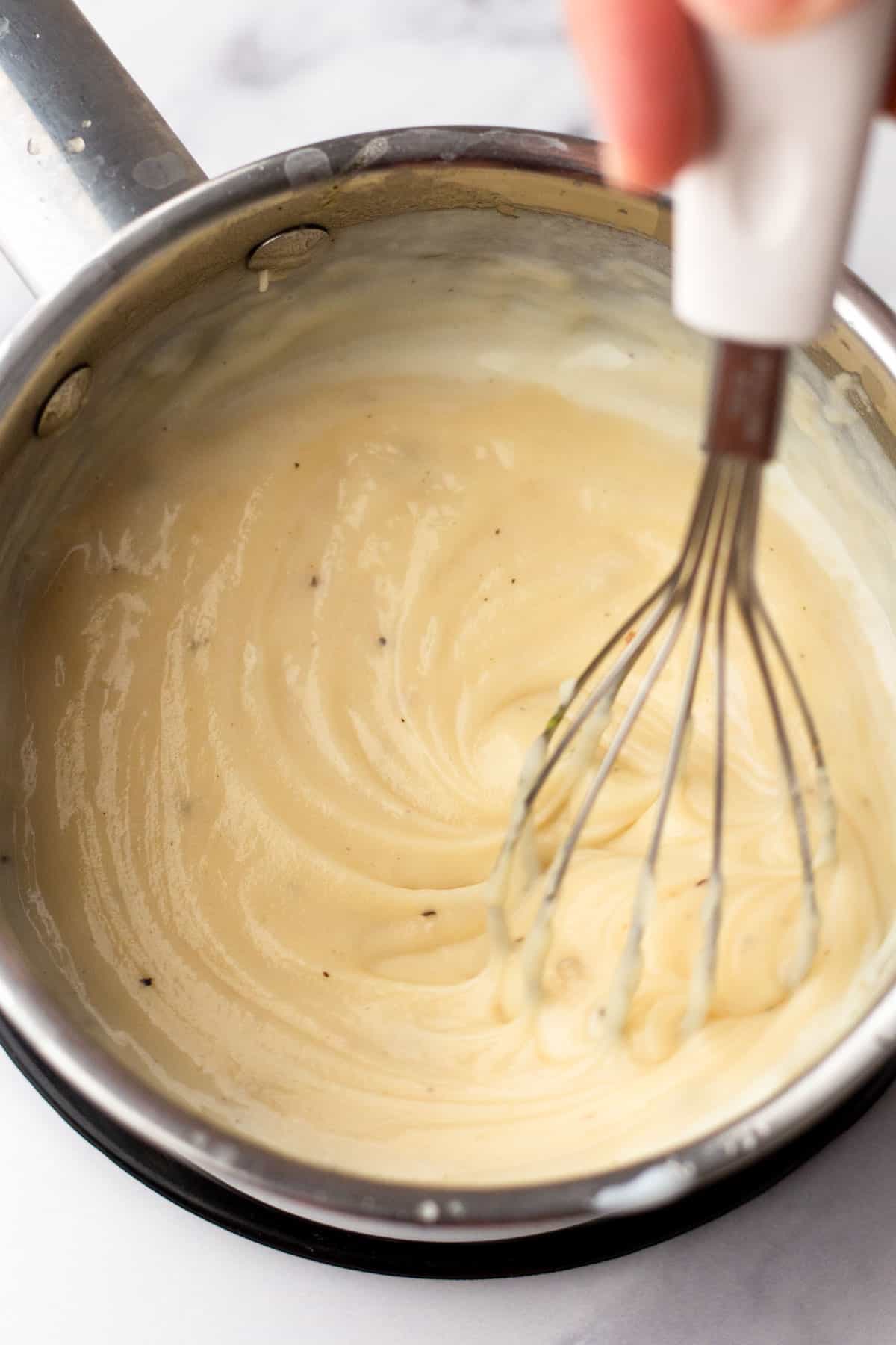 A person whisks cream of chicken in a saucepan on a stove.