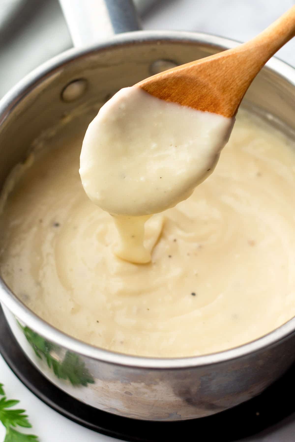 A wooden spoon holds thick, creamy cream of chicken above a saucepan filled with more soup.