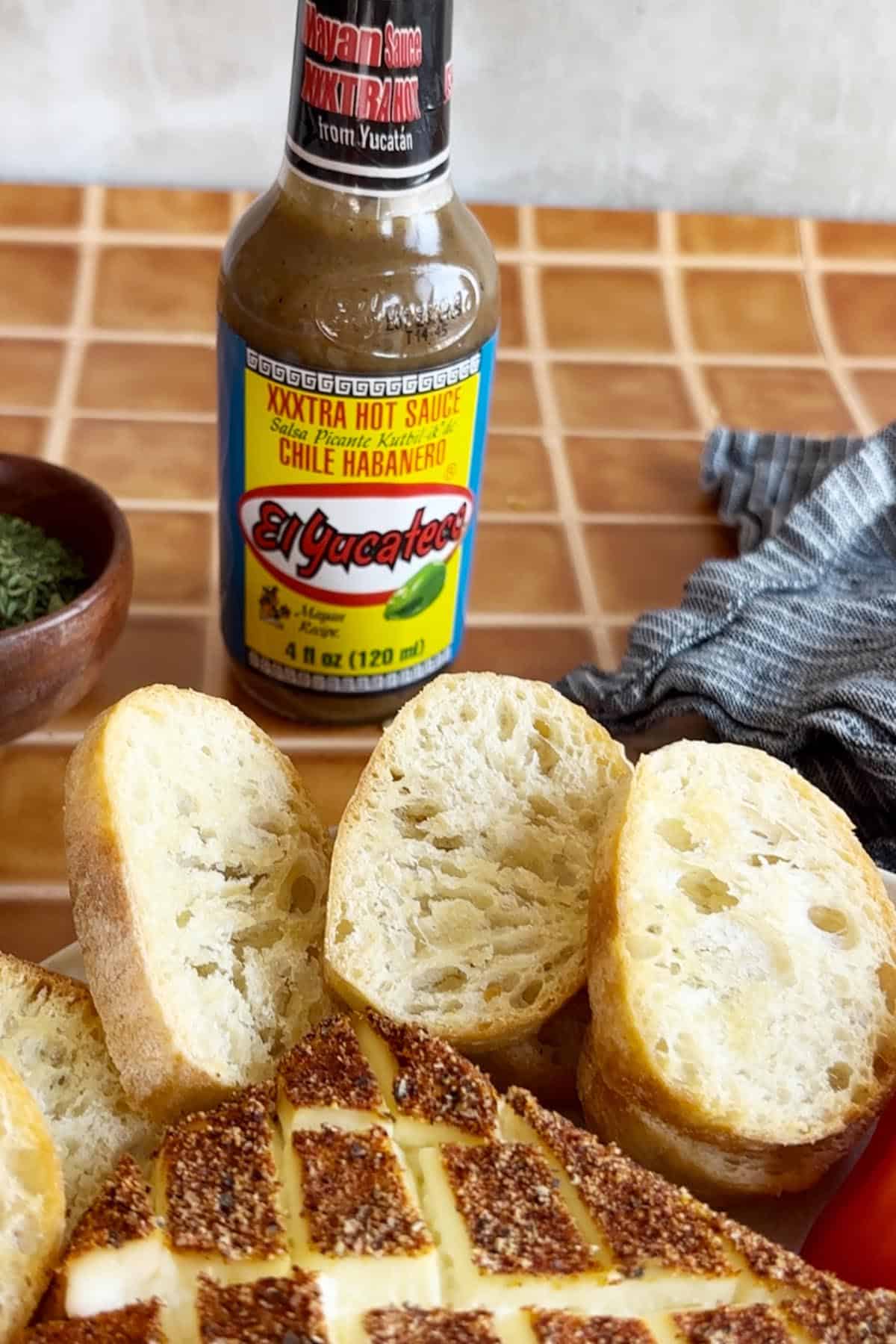 Sliced bread and smoked cream cheese sit on a table alongside a bottle of El Yucateco XXXtra Hot Sauce, adding a fiery touch.