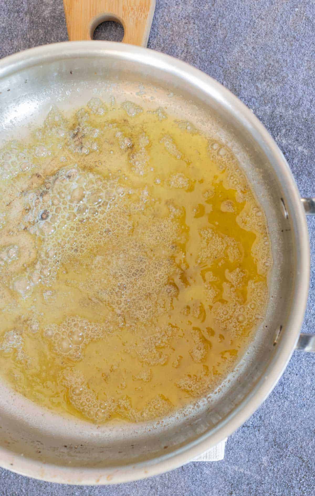 A stainless steel pan with bubbling melted butter on a gray surface.