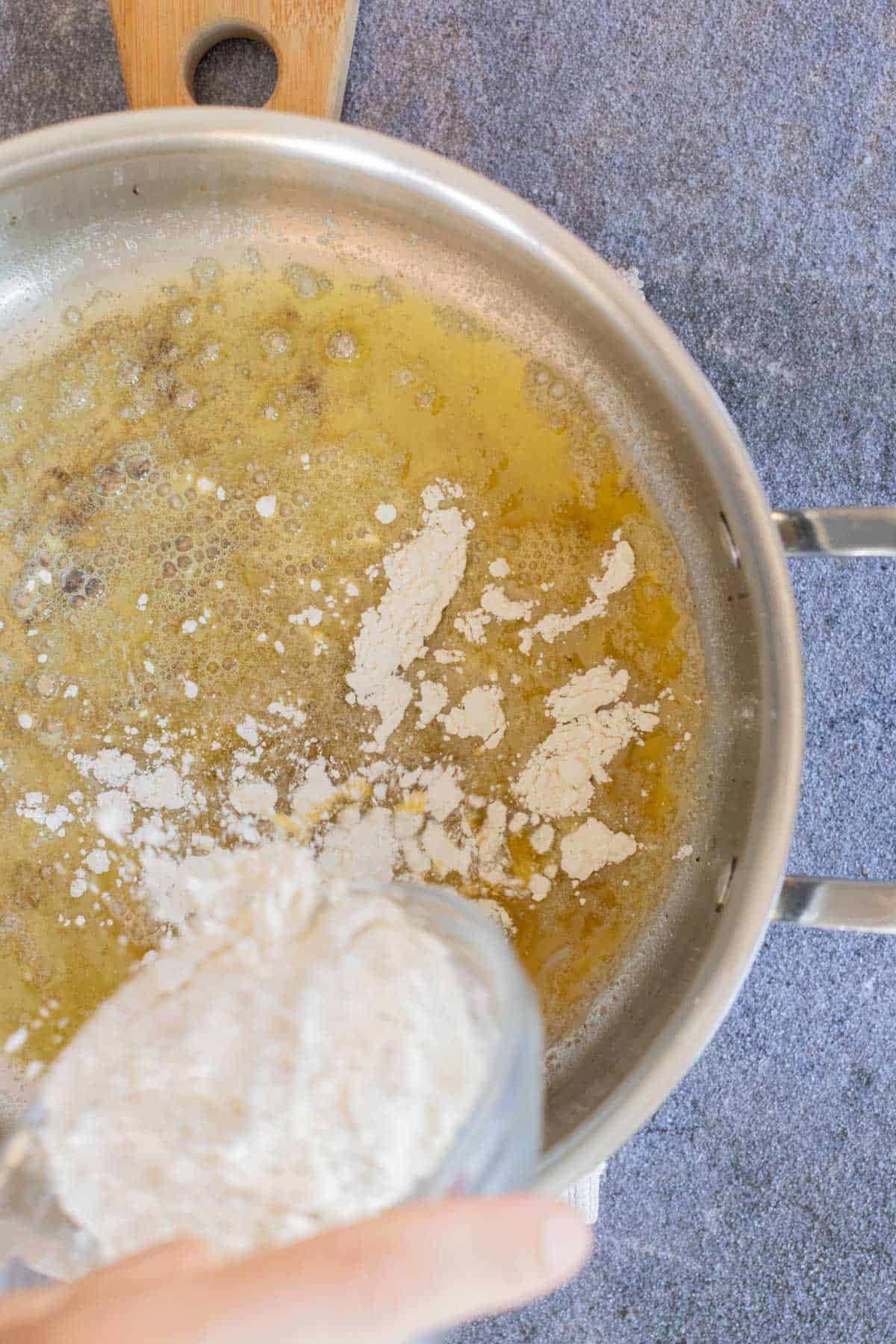 A skillet on a stove with melted butter and flour being added from a measuring cup, appearing to start a gravy.