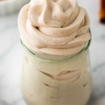 A jar of pumpkin-spiced whipped cream with a swirl. A small dish with cinnamon is visible in the background.