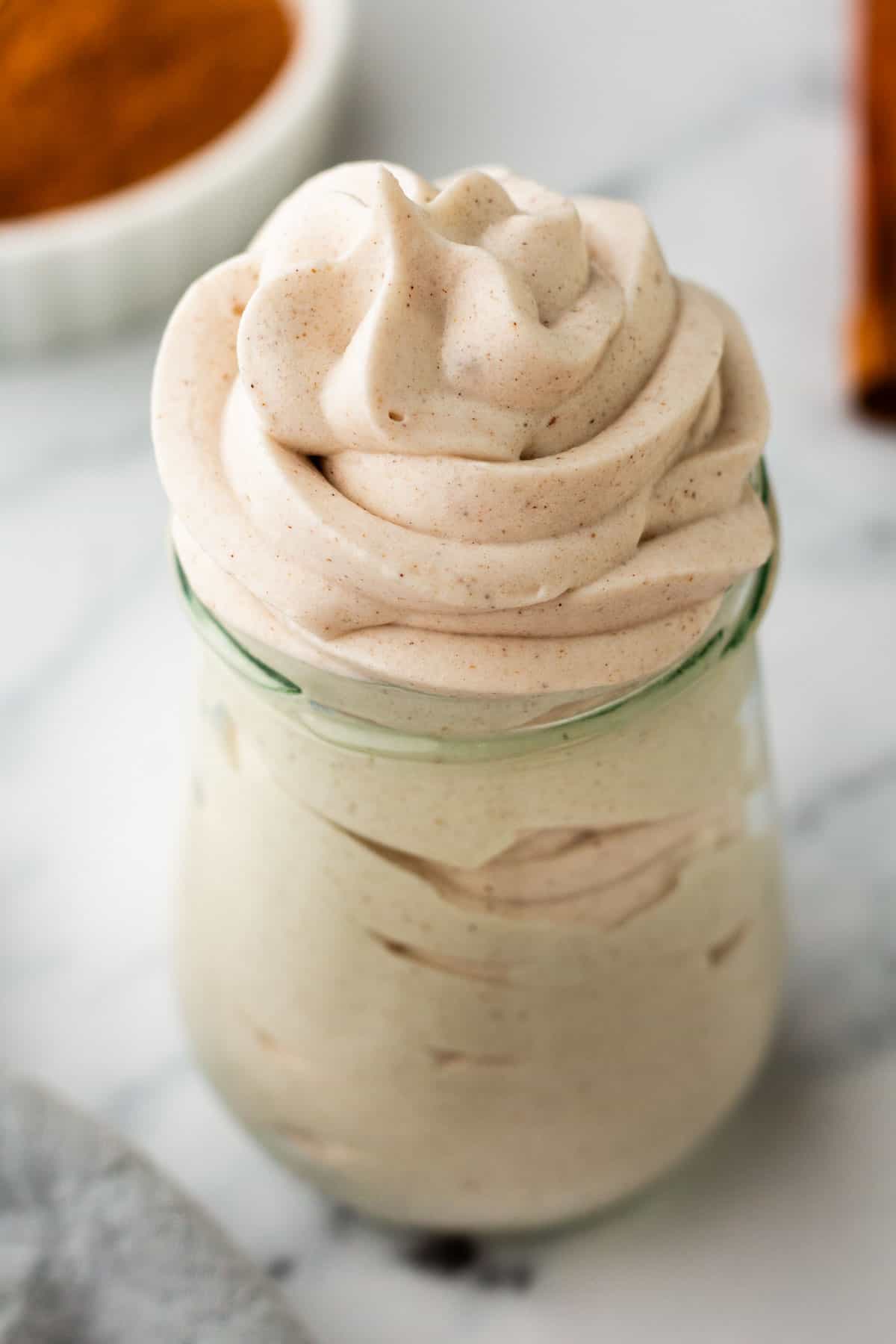 A jar of pumpkin-spiced whipped cream with a swirl. A small dish with cinnamon is visible in the background.