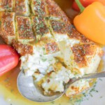 Smoked cream cheese with a golden, seasoned crust, garnished with herbs, surrounded by sliced bread and peppers, with a spoon scooping some cheese.