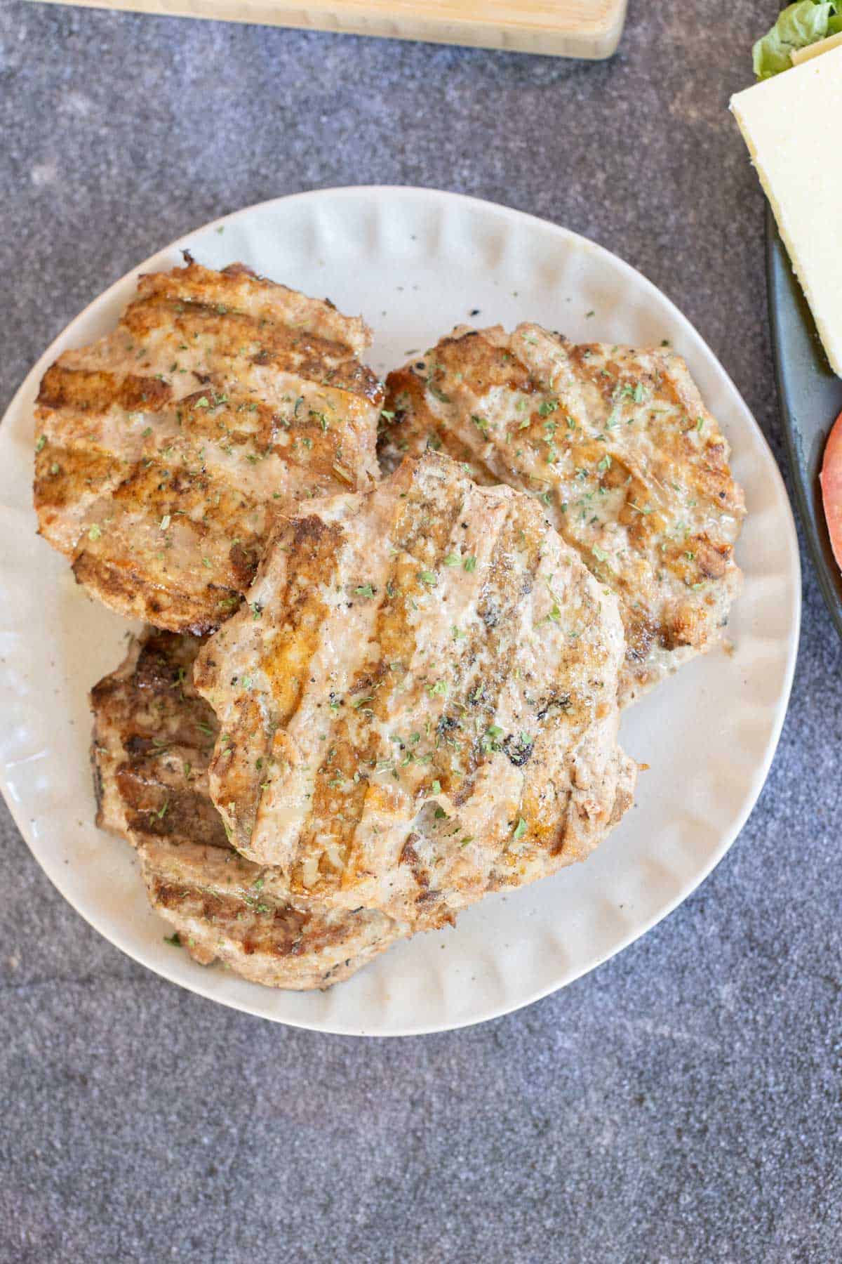 Grilled turkey burgers stacked on a white plate, placed on a gray countertop.