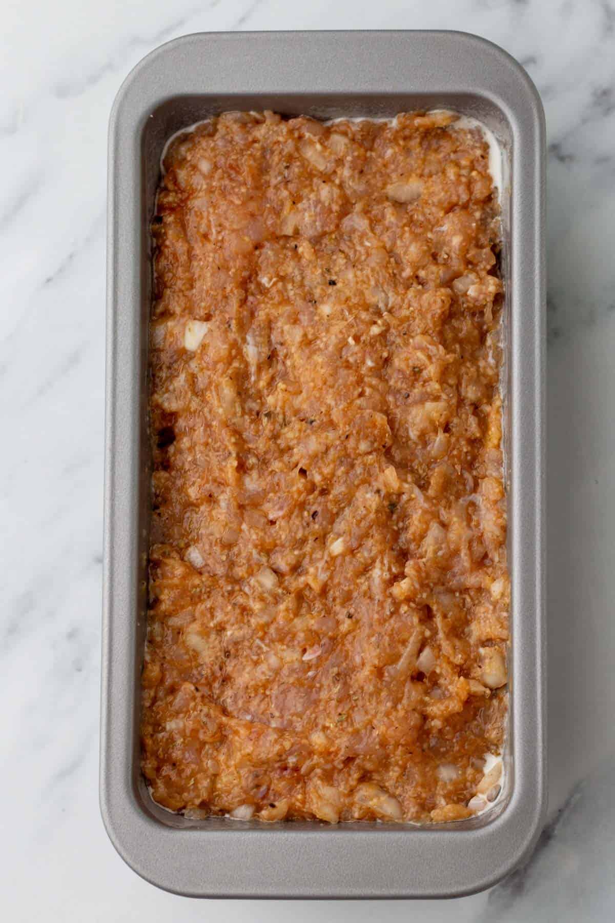 Raw turkey meatloaf mixture in a rectangular baking pan on a marble surface.