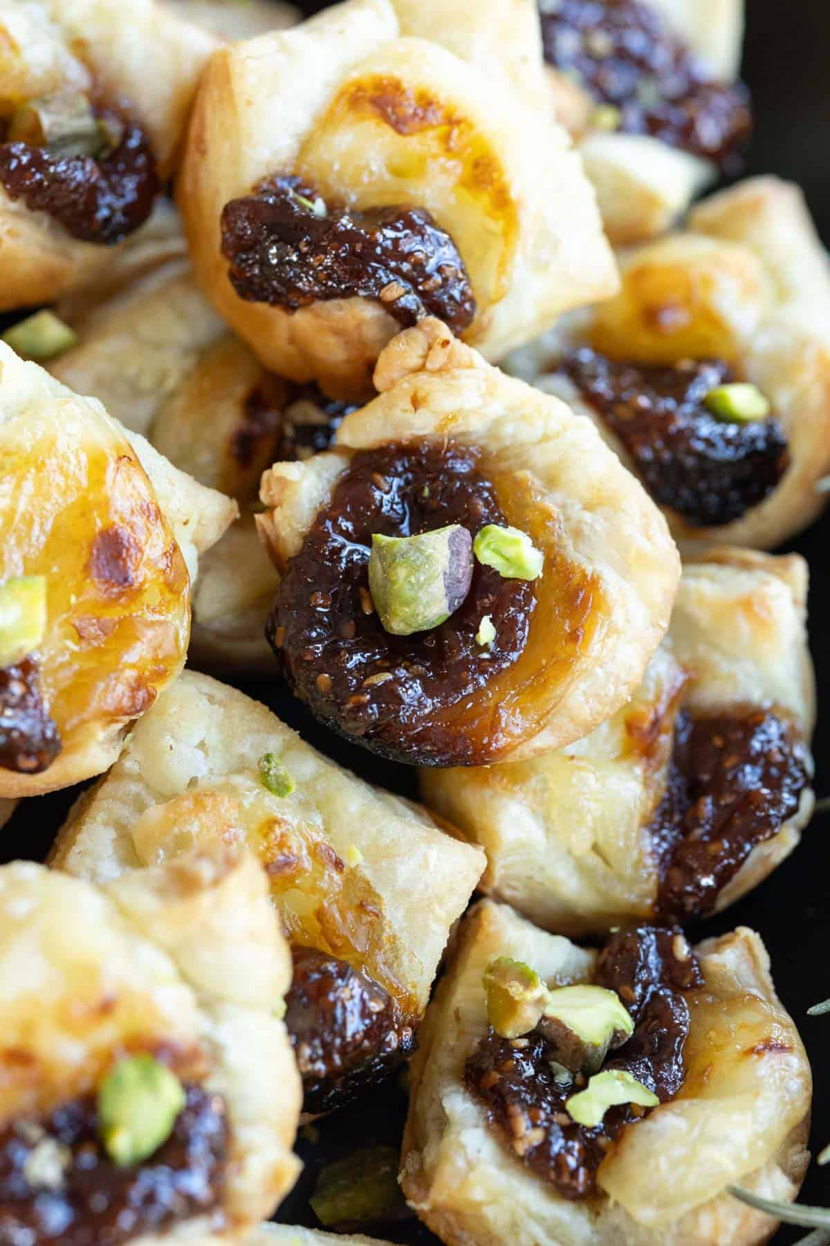 Close-up of puff pastry bites filled with fig jam and topped with pistachio pieces.