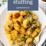A plate of savory cornbread stuffing, garnished with fresh herbs, rests elegantly beside a gleaming gold fork.