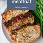 Generous slices of turkey meatloaf garnished with herbs, elegantly served alongside fresh green beans on a pristine plate.