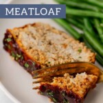A mouthwatering slice of turkey meatloaf rests on a plate with crisp green beans, partially cut with a fork and knife.