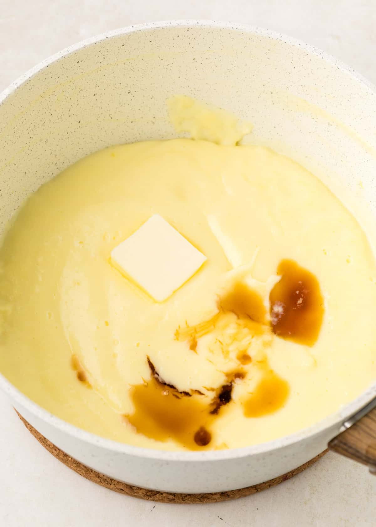 A saucepan containing creamy sauce with a pat of butter and a splash of vanilla extract added on top.