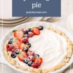 A luscious vanilla pudding pie garnished with fresh strawberries, blueberries, and a dusting of powdered sugar sits elegantly on a light background, accompanied by nearby plates.