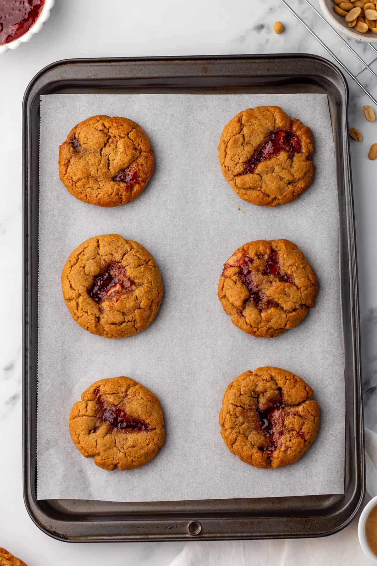 A baking tray with six peanut butter and jelly cookies on parchment paper.