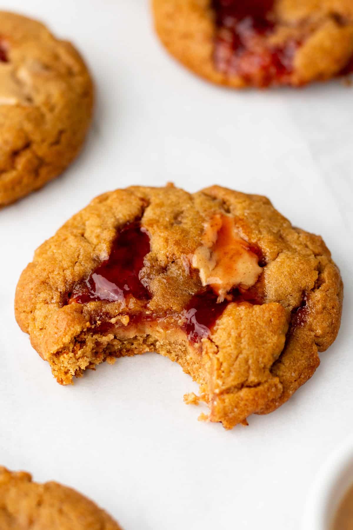 Close-up of a peanut butter and jelly cookie with a bite taken out, displaying the jelly filling.