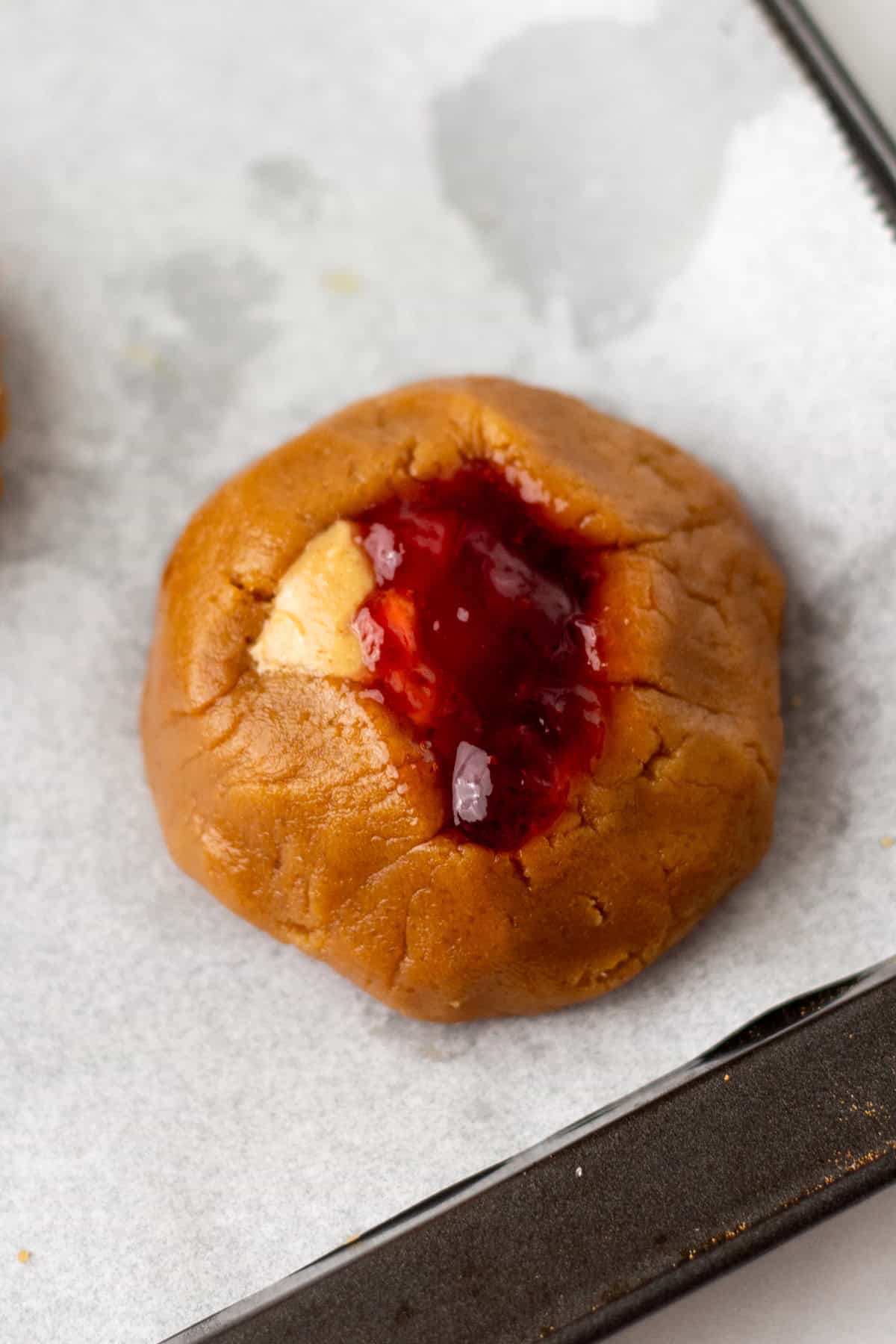 A cookie with a red jam center on a baking tray lined with parchment paper.