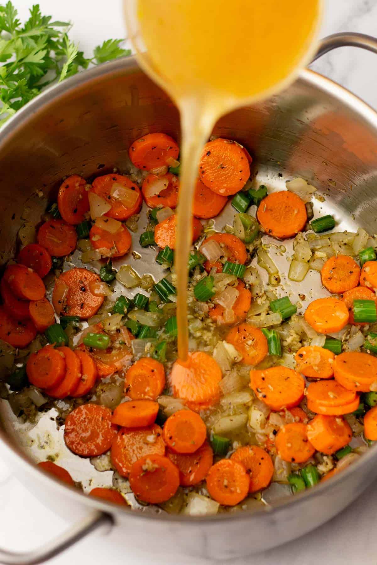 Carrots, onions, and green onions in a pot with broth being poured in.