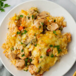 A plate of chicken and rice casserole with melted cheese and vegetables, garnished with parsley.