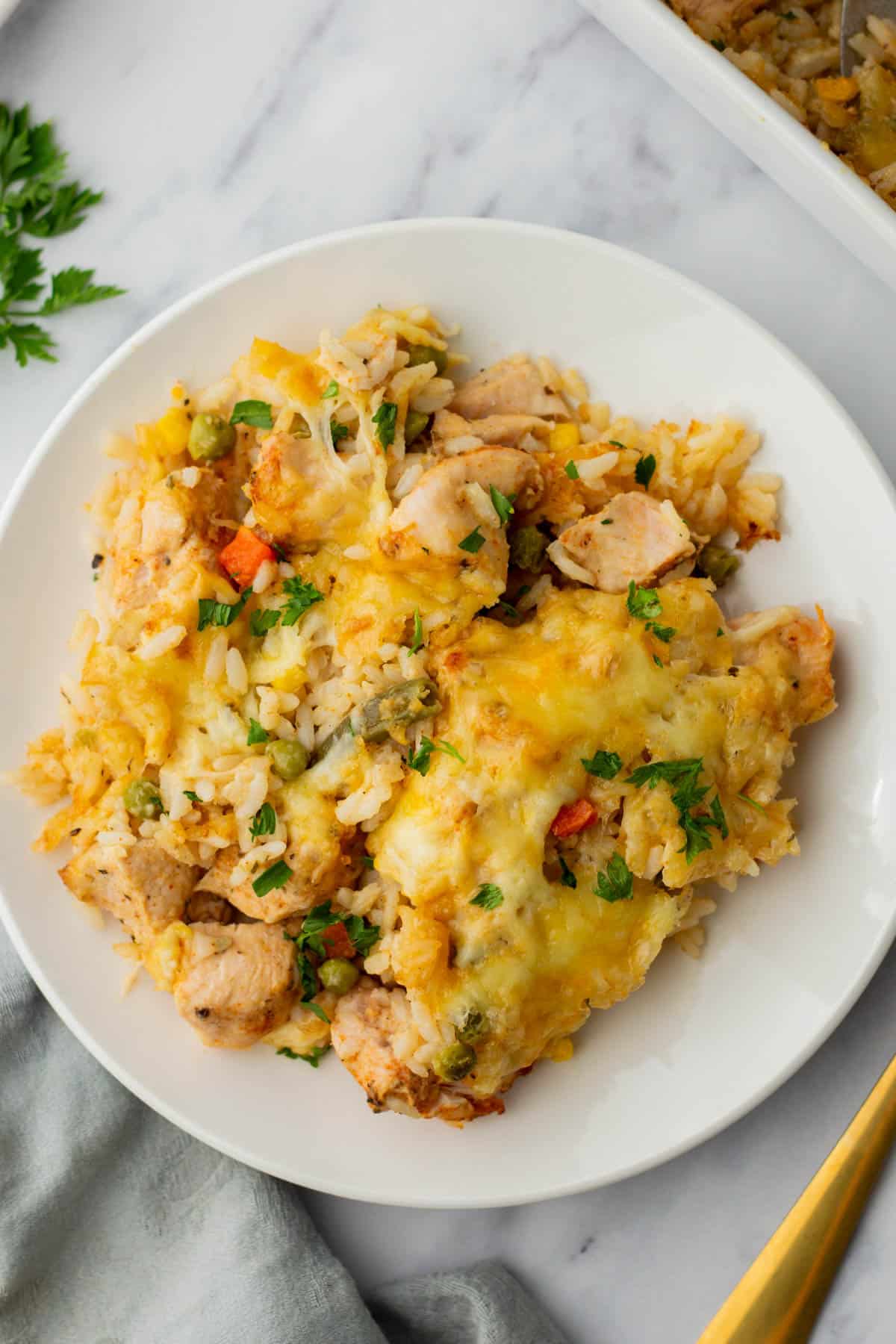 A plate of chicken and rice casserole with melted cheese and vegetables, garnished with parsley.
