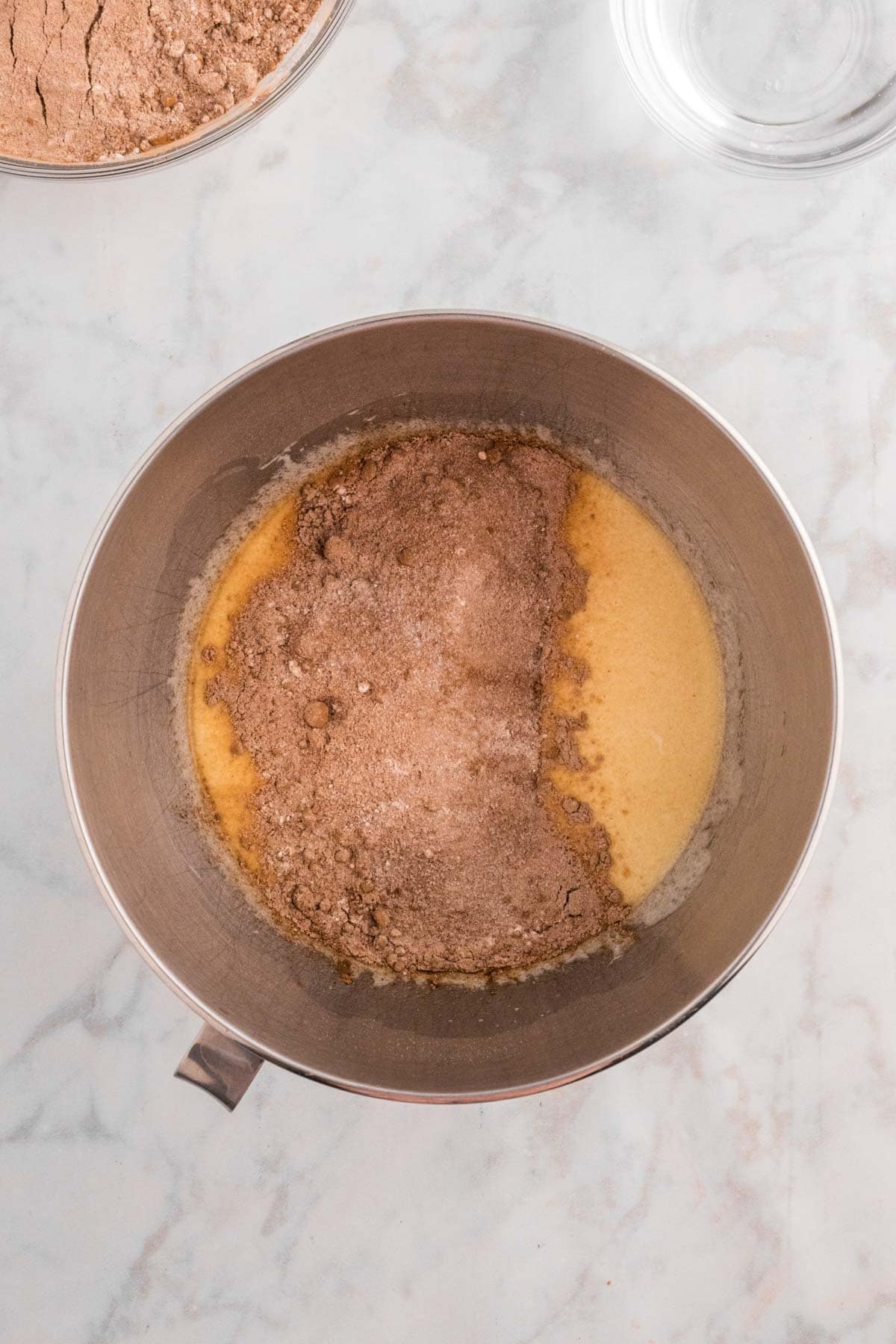 A mixing bowl with flour and liquid ingredients, partially combined, on a marble countertop.