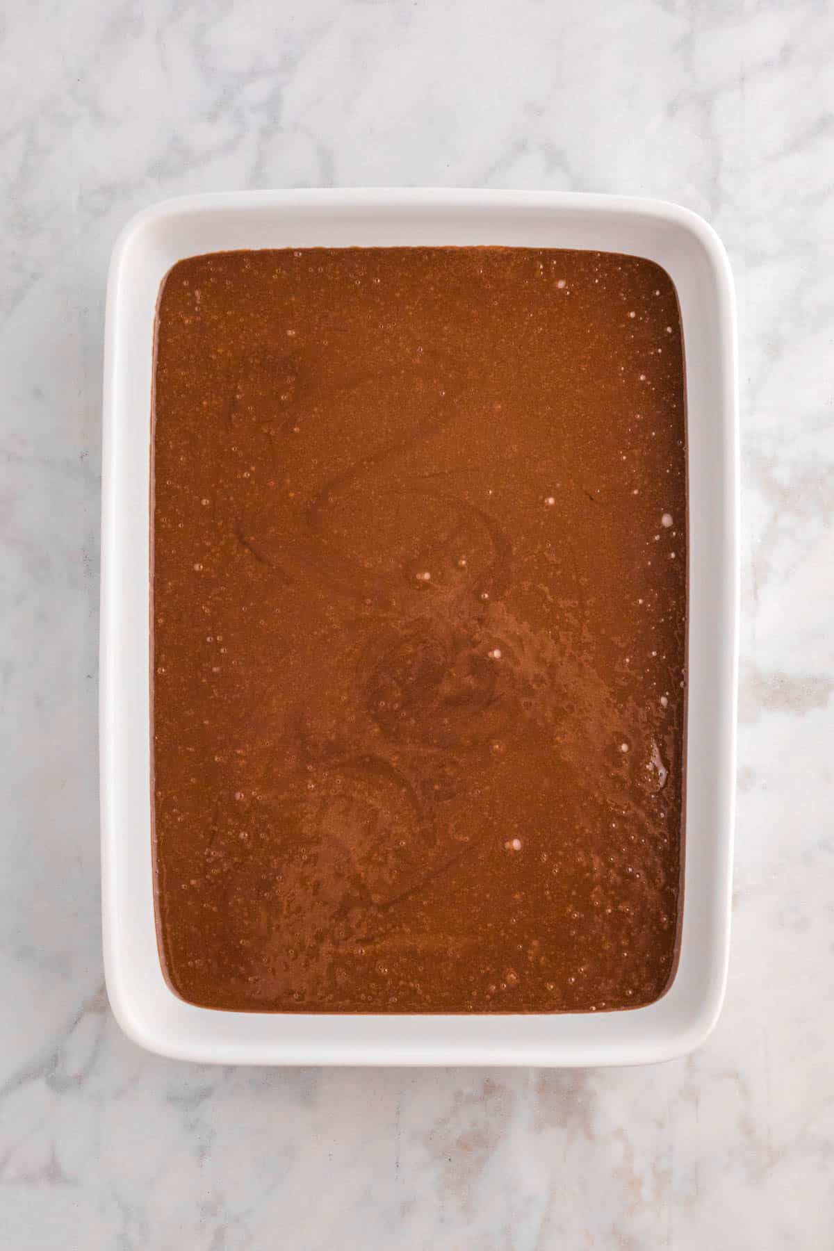 A rectangular white baking dish filled with chocolate batter on a marble surface.