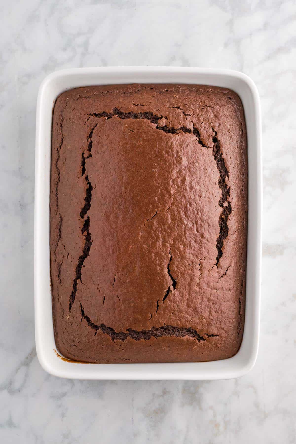A baked chocolate cake in a rectangular white dish on a marble surface.