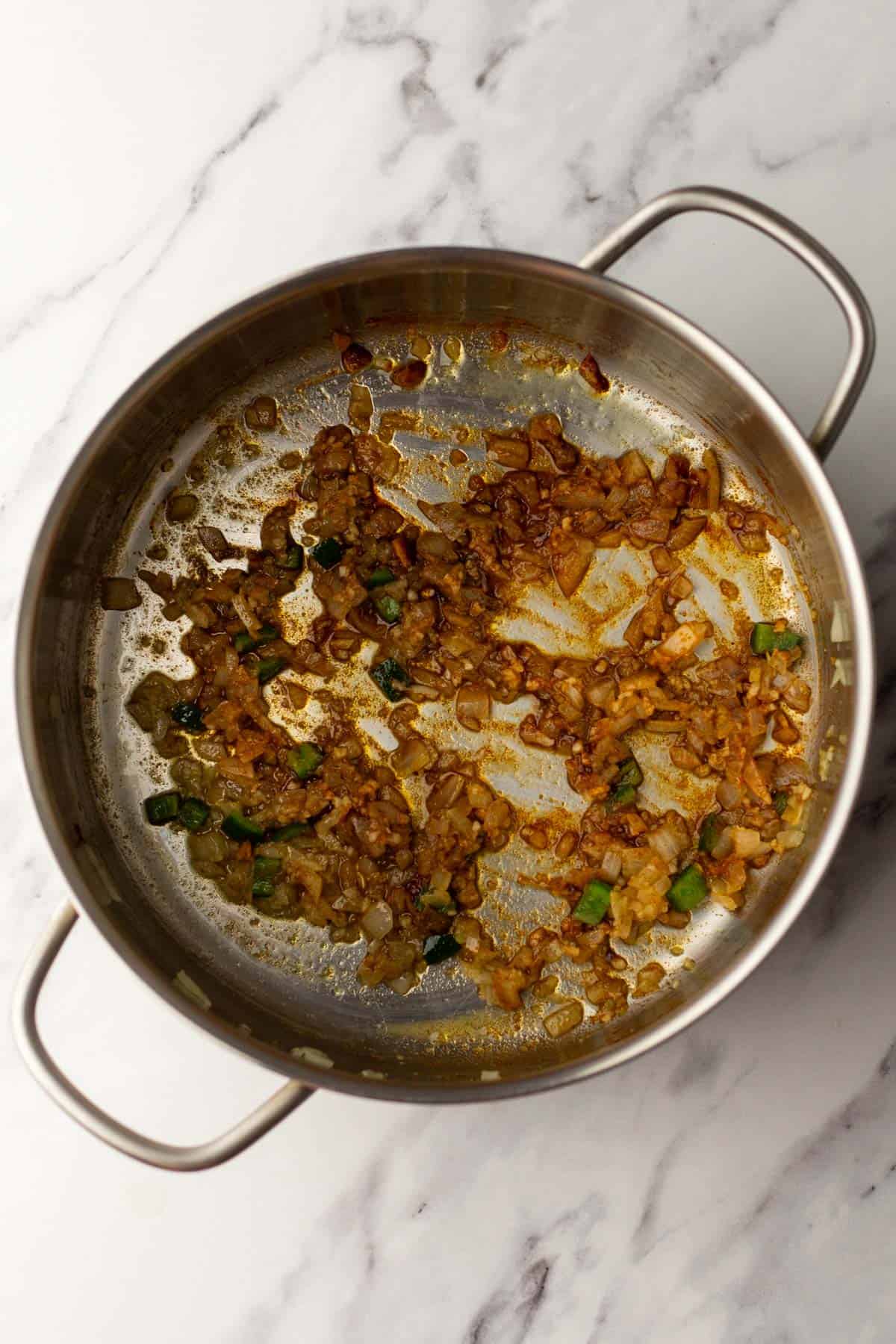 Saut&eacute;ed onions and peppers in a stainless steel pot on a marble countertop.