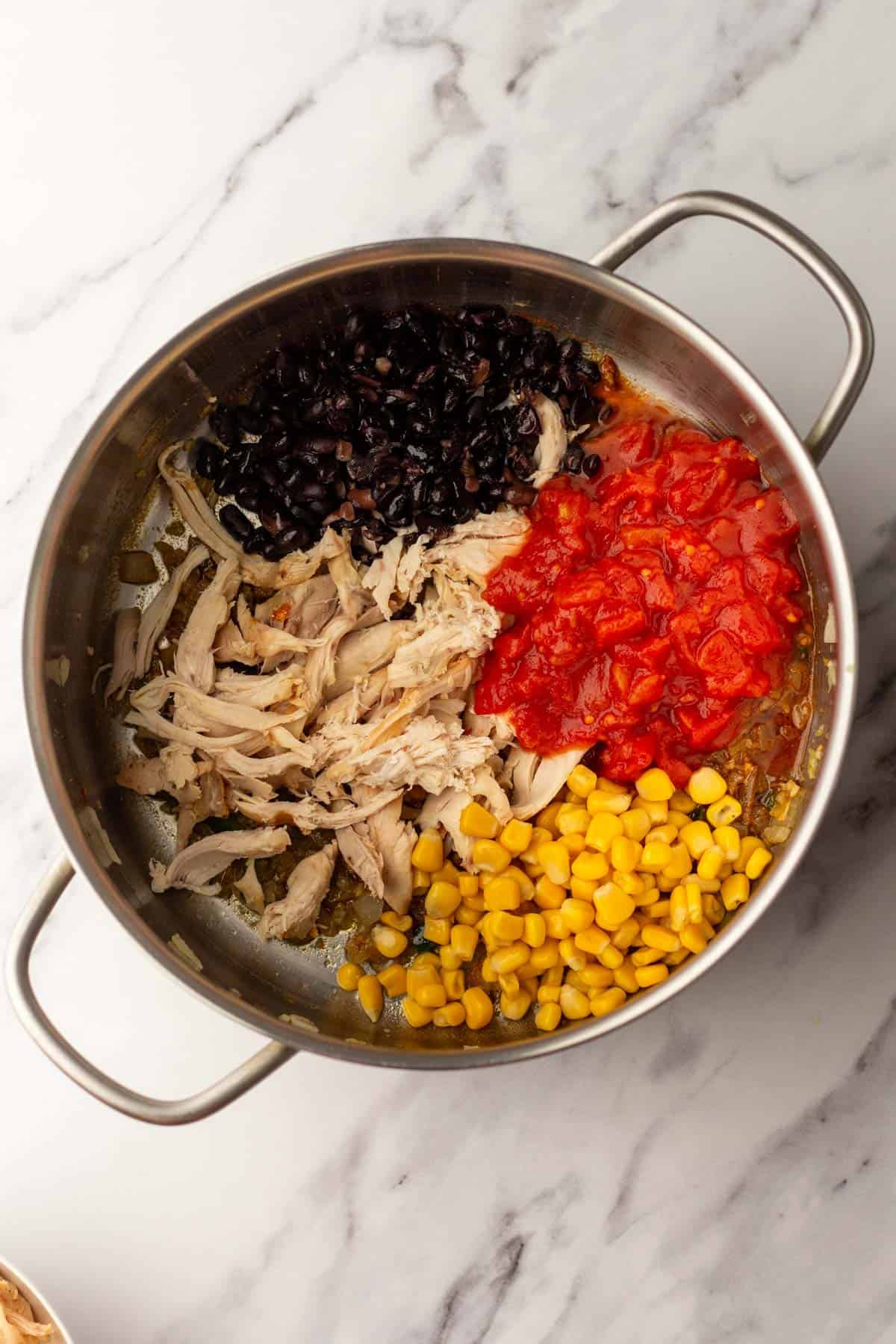 A pot on a marble surface contains shredded chicken, black beans, diced tomatoes, and corn.