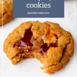 A peanut butter cookie with a bite taken, revealing a delightful jelly filling, reminiscent of ginger cookies. The text at the top reads, "peanut butter and jelly cookies joyfullymad.com".
