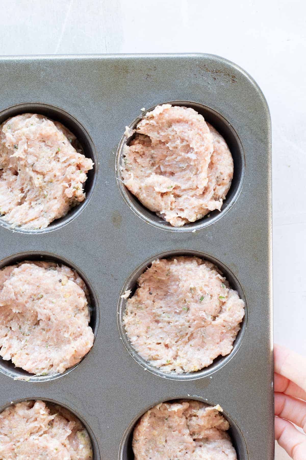 Raw ground meat mixture pressed into a metal muffin tin, ready for cooking.