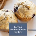 Two banana blueberry muffins rest on a plate, accompanied by two fragrant cinnamon sticks.